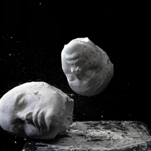 Drei weiße Gipsmasken fliegen durch die Luft, umgeben von Staub und Bruchstücken – ein kraftvolles Bild für Identität, Wandel und kreative Mediengestaltung.